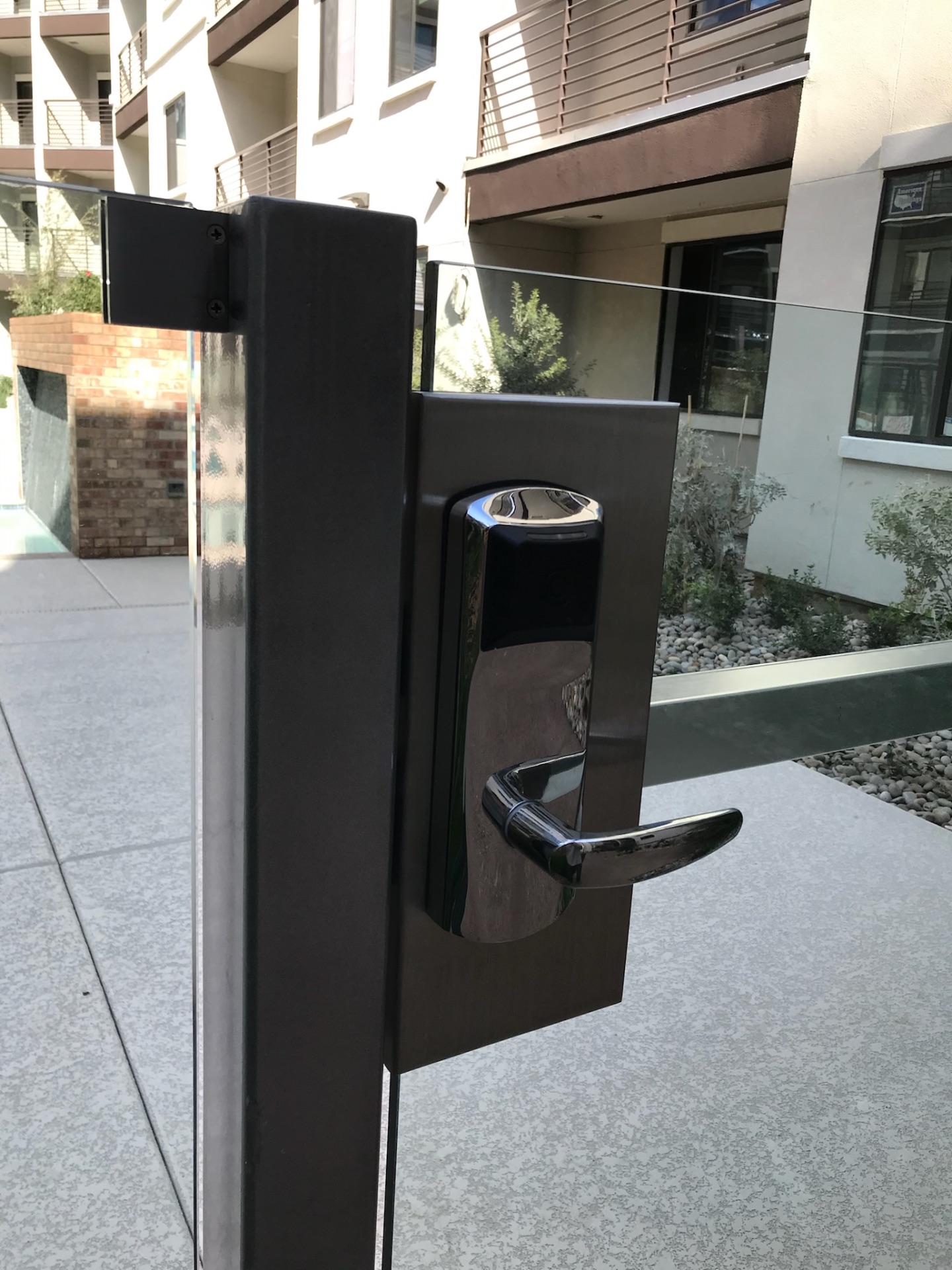 Electronic access hardware on a dark-finished commercial glass fence gate post at a Phoenix apartment pool enclosure.