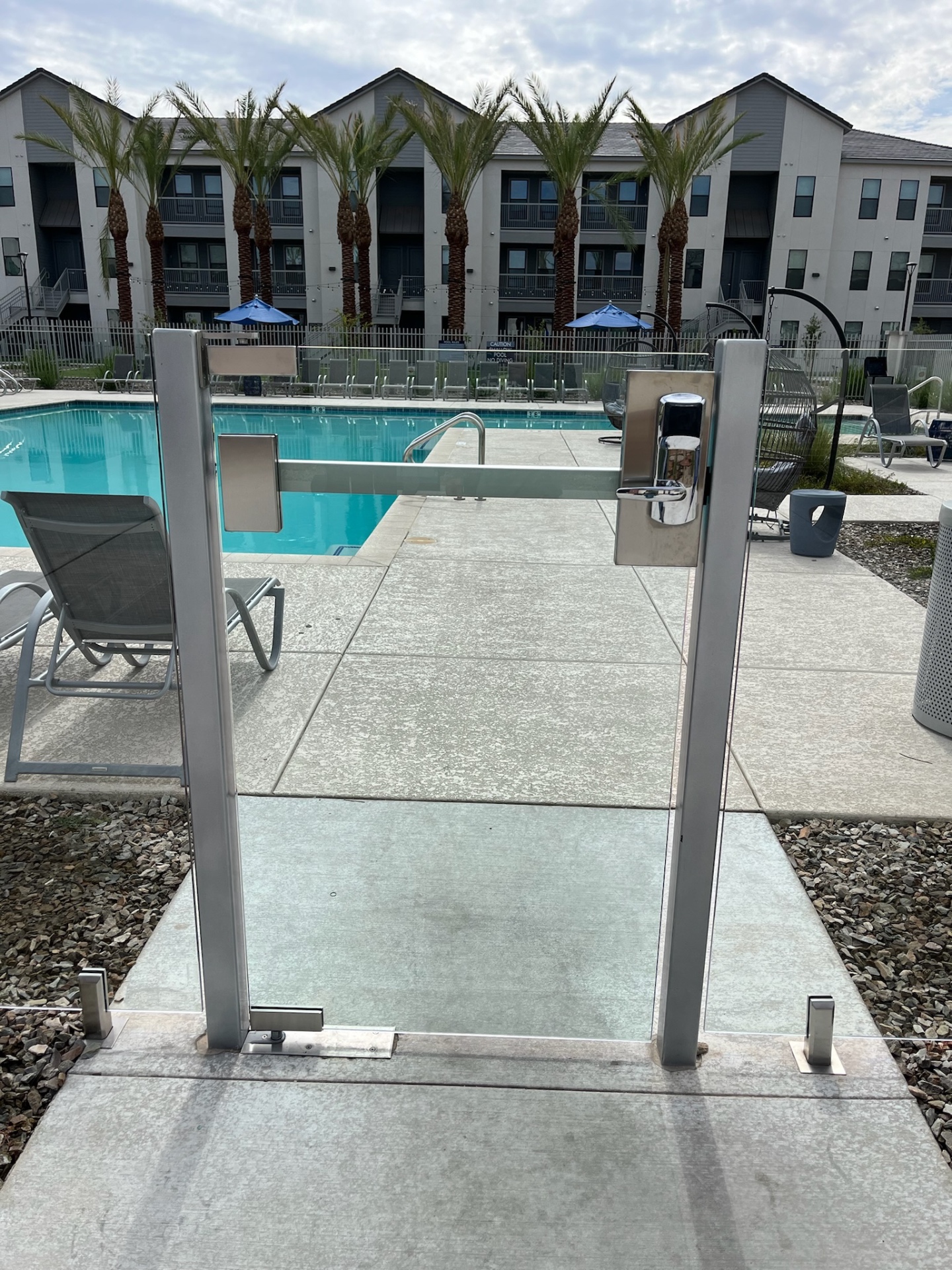 Close-up of a commercial glass fence gate assembly with access-control hardware at a resort-style Arizona apartment pool.