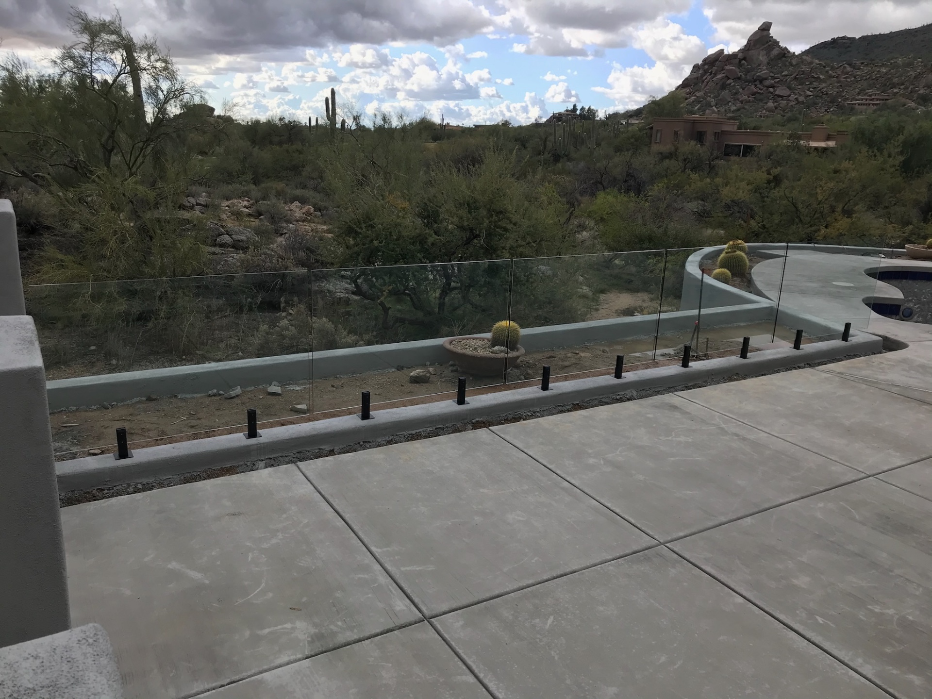 Frameless glass fence panels following a curved bond beam around a desert pool — glass fencing in Arizona with mountain and saguaro views.