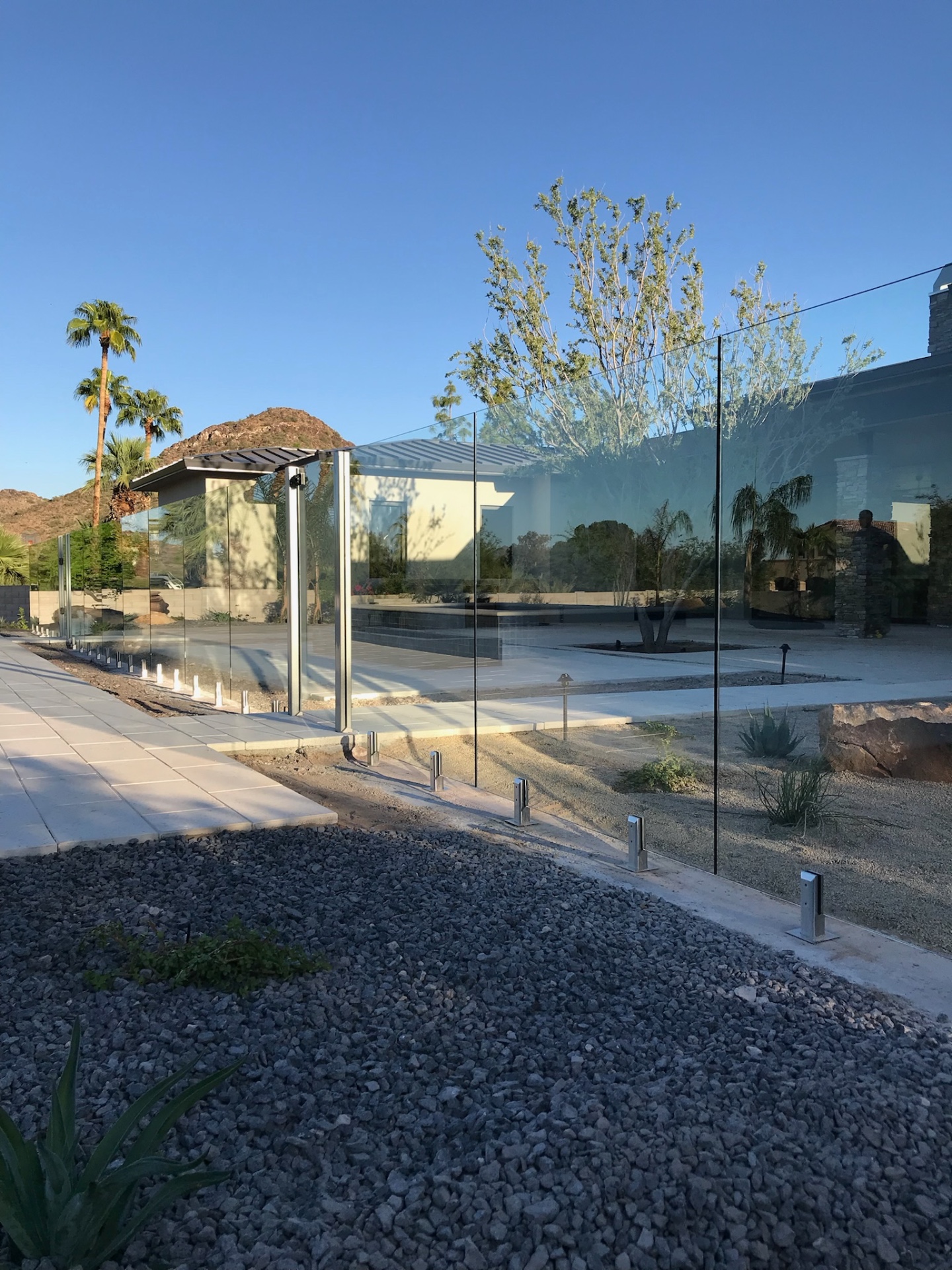 Crystal-clear sightlines through tempered glass fence panels showing desert hills and palm trees beyond a Scottsdale pool deck — glass fencing in Arizona.