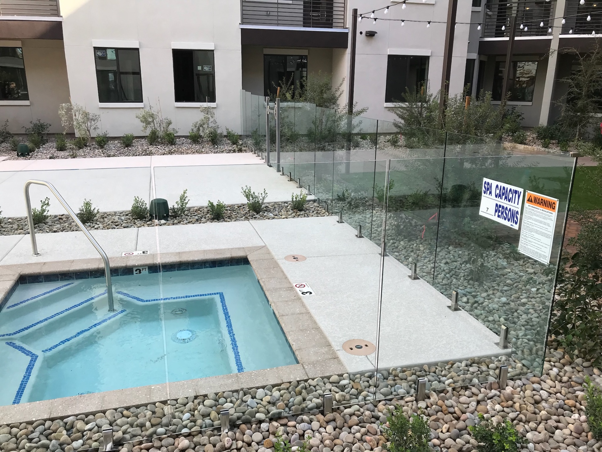 Commercial frameless glass fencing protecting a spa area with required capacity and warning signage visible on the glass fence panels.