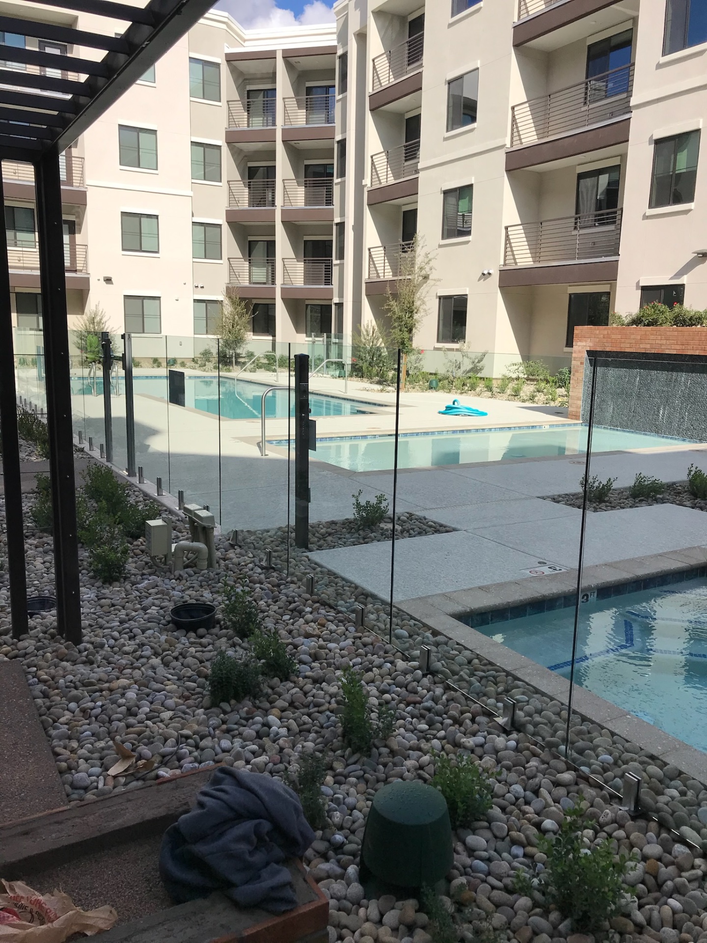 Commercial glass fence panels running past a spa and pool with metal canopy structure and multifamily residences in the background — Arizona glass fencing.