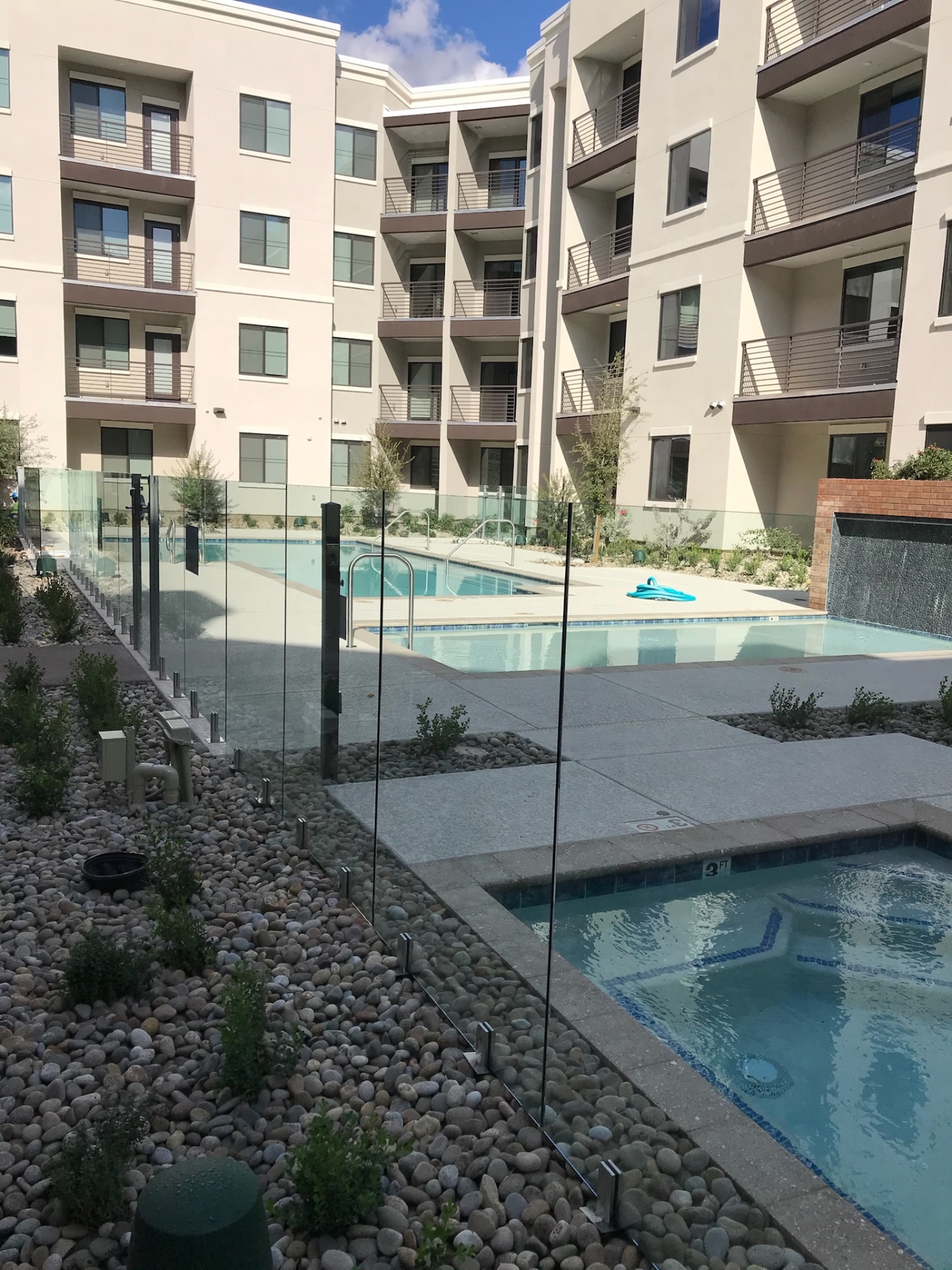 Wide view of a multifamily pool amenity enclosed with commercial frameless glass fence panels and black access gate posts in Phoenix.