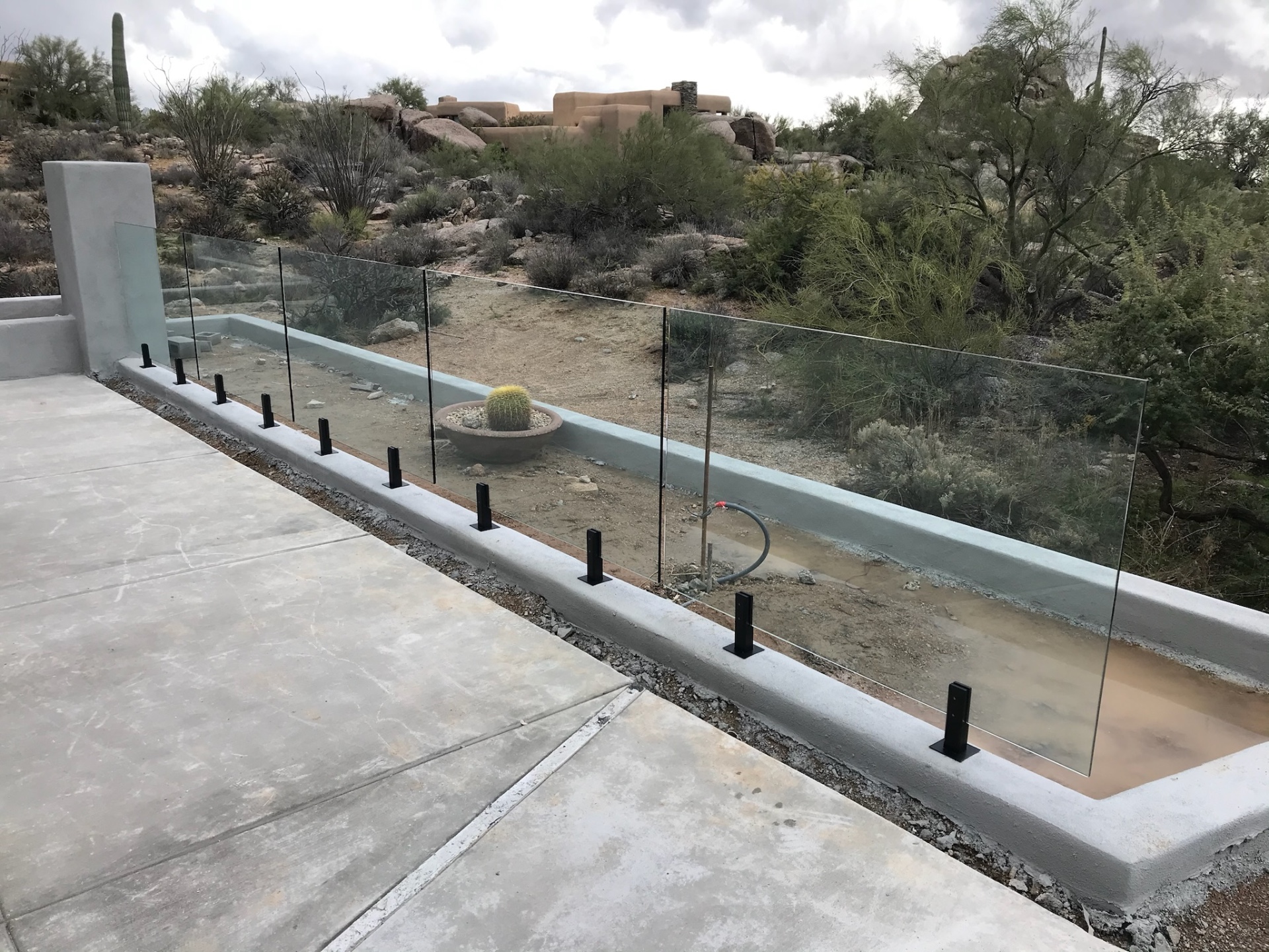 Straight run of tempered glass fence panels along a Sonoran Desert pool deck — Arizona glass fencing with saguaros and Pueblo-style homes in the distance.