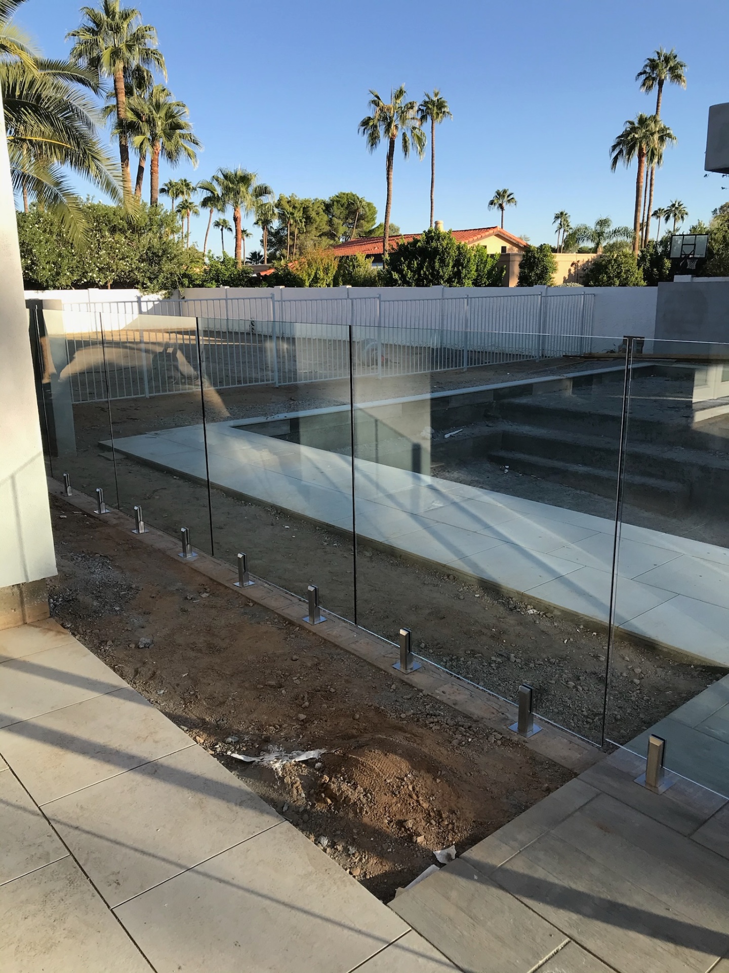 Glass fence panels on stainless spigots along a freshly poured pool deck with palms and mature landscape behind an Arizona property.