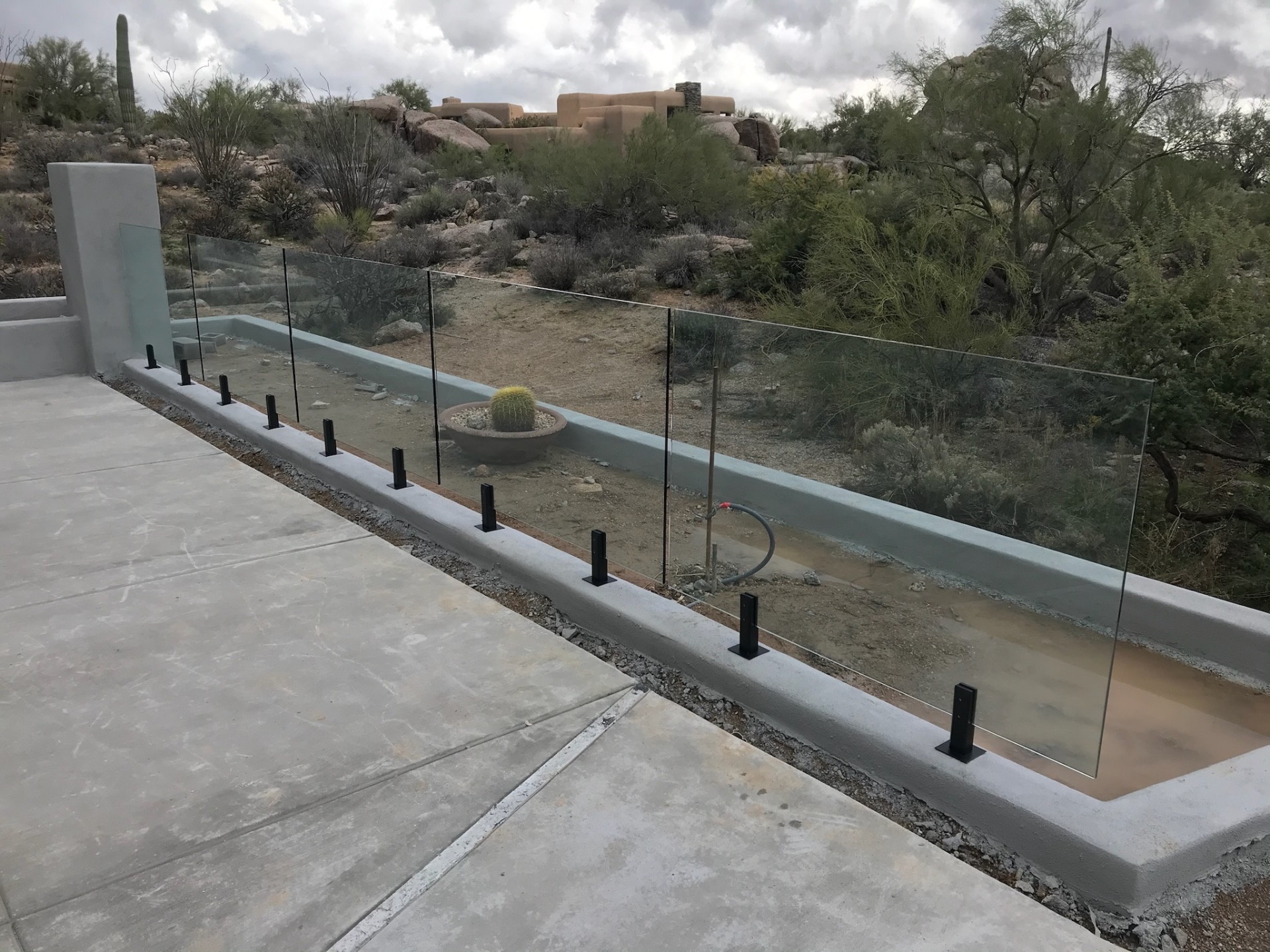 Glass fence panels with black stainless spigots anchored into a poured-in-place bond beam at a North Scottsdale glass fencing project.