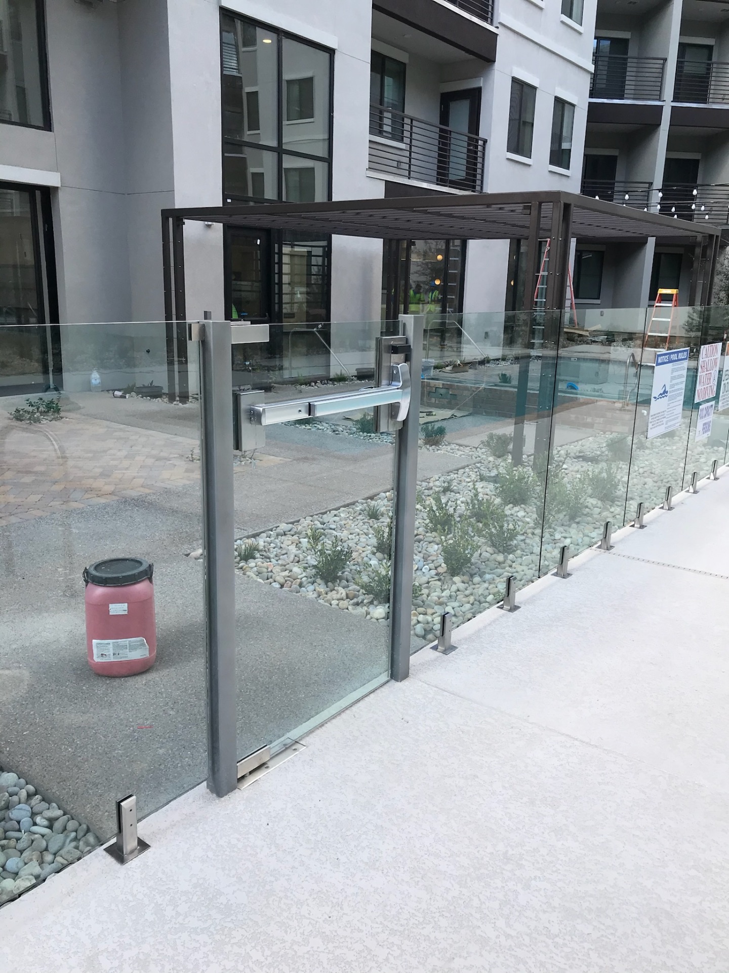 Commercial glass fence gate with panic hardware and steel shade structure at a multifamily amenity pool — commercial glass fencing in Arizona.