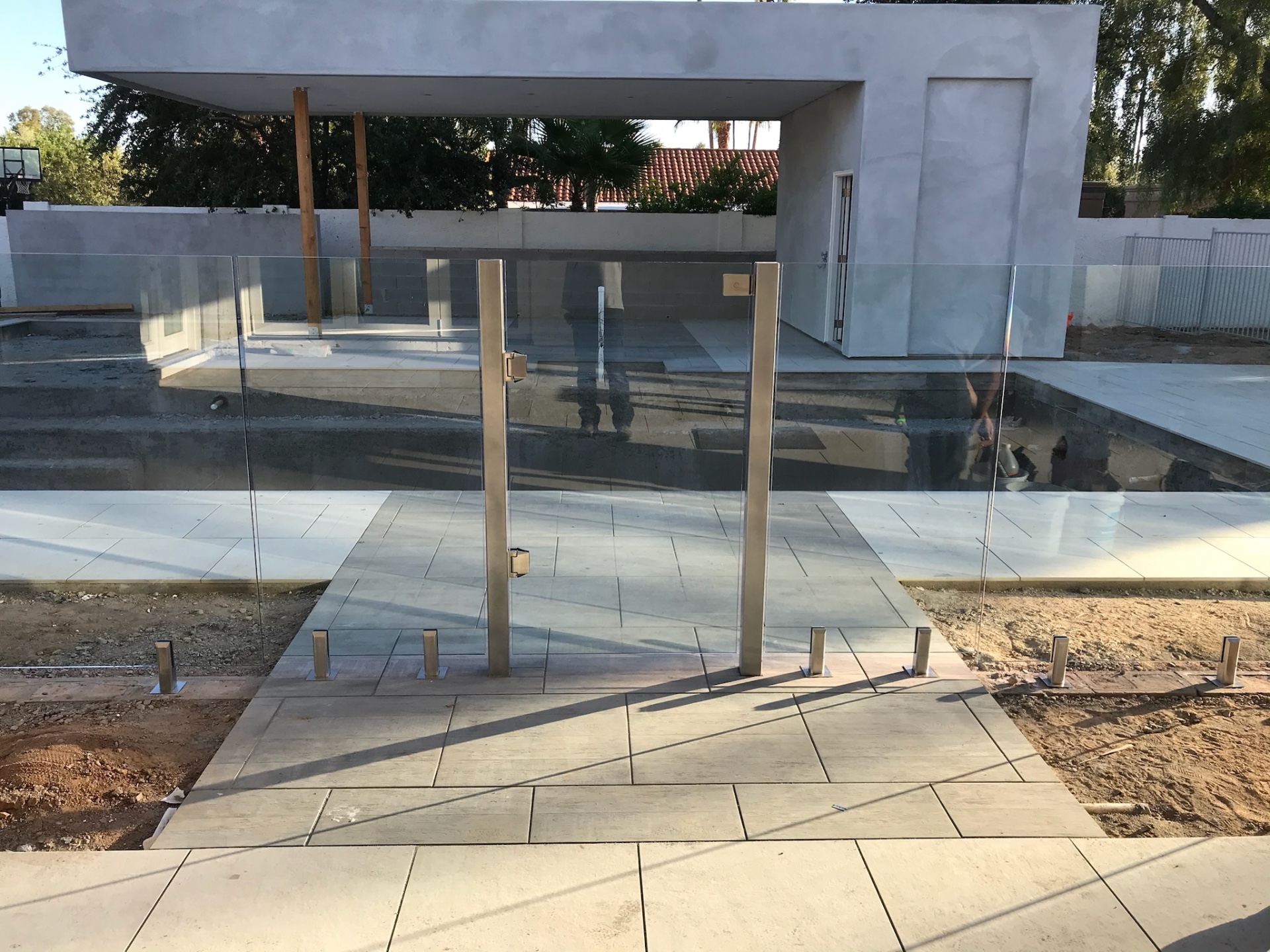 Glass fence panels with self-closing gate set between brushed stainless gate posts, mounted into porcelain pavers around a new Arizona pool.