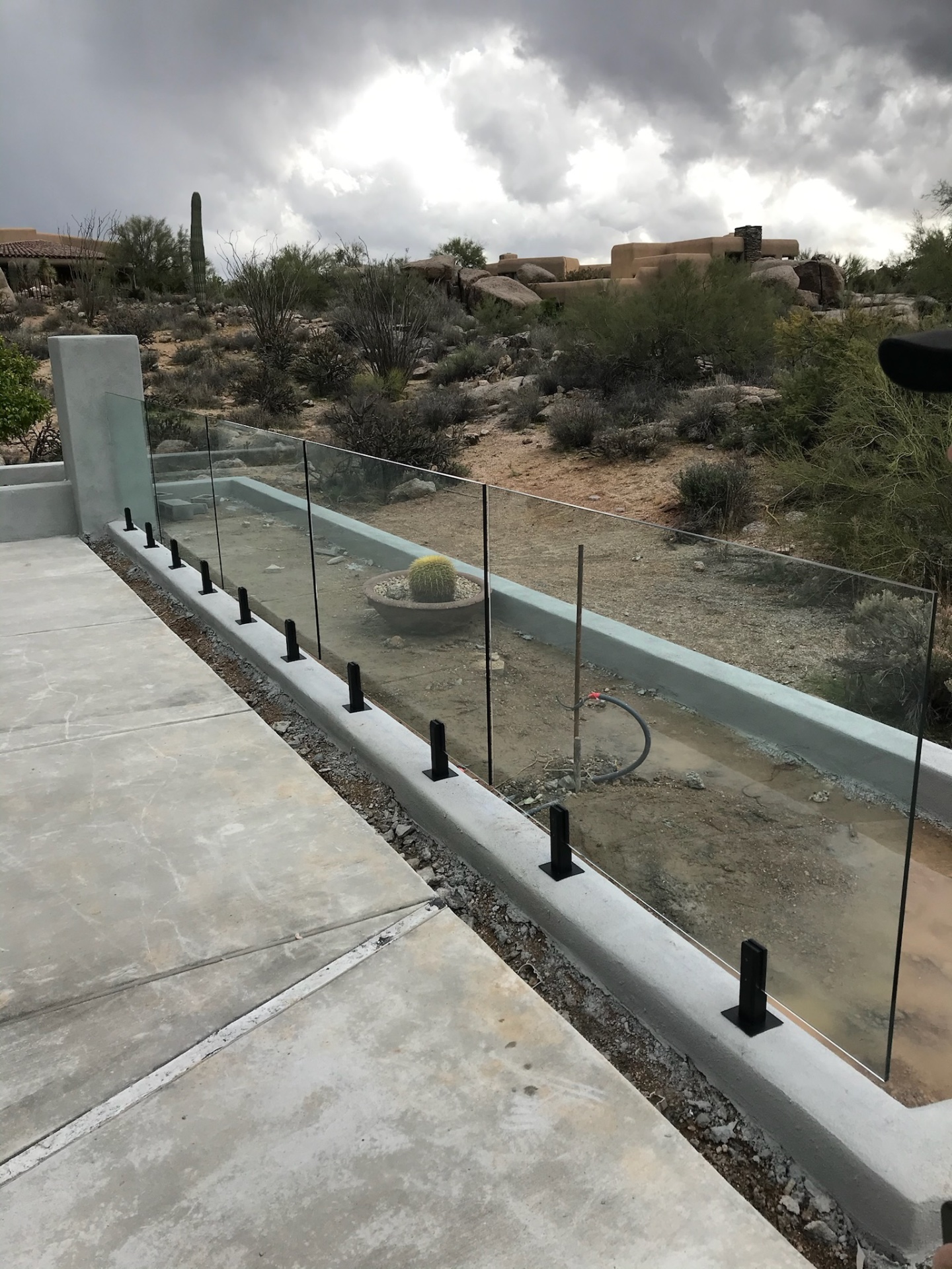 Frameless glass fence pool barrier viewed from the deck side — clean sightlines through tempered glass panels to the natural Sonoran Arizona landscape.