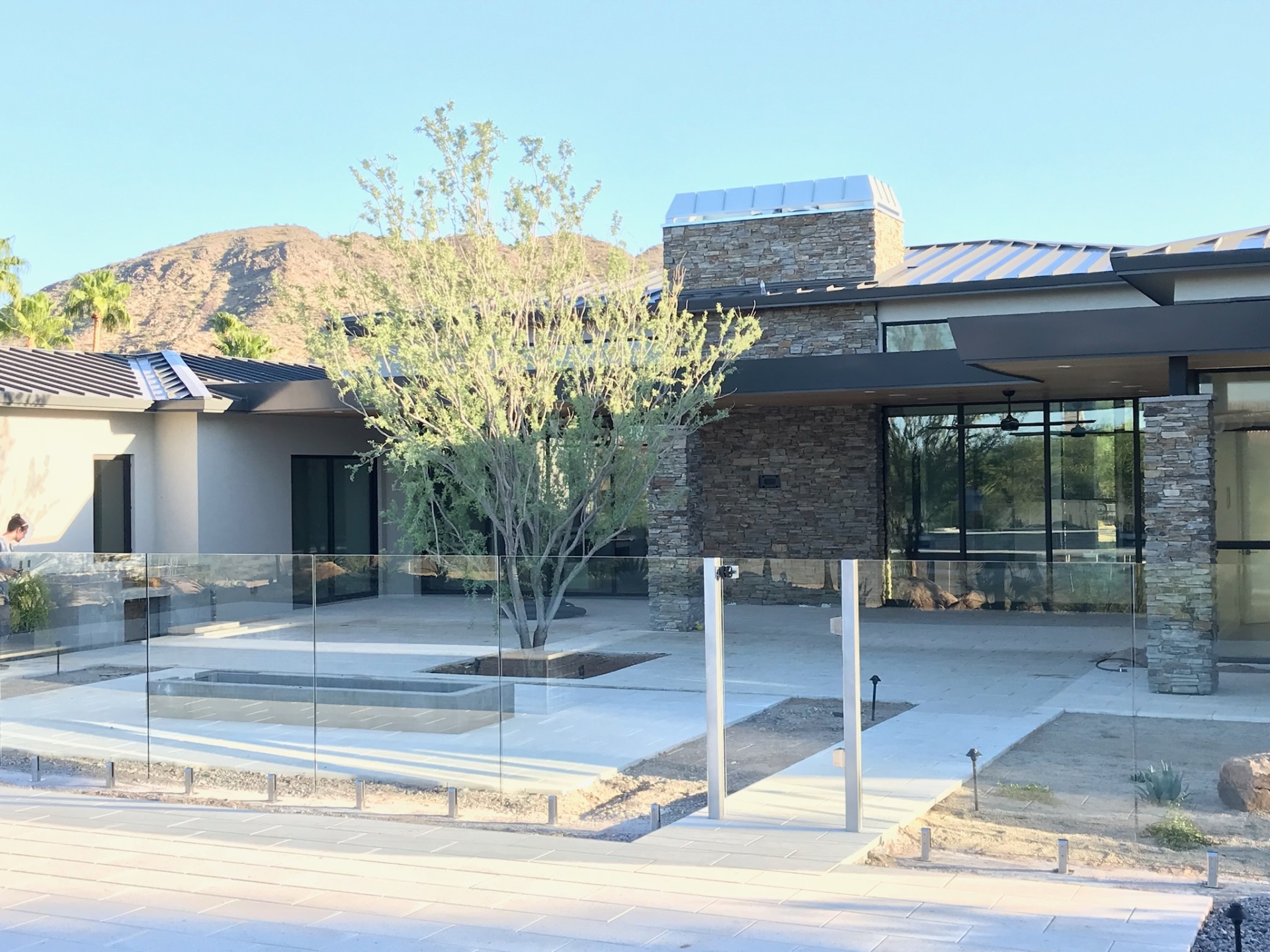 View across porcelain pavers framing the custom home patio, outdoor living space, and code-conscious frameless glass fence pool barrier in Arizona.