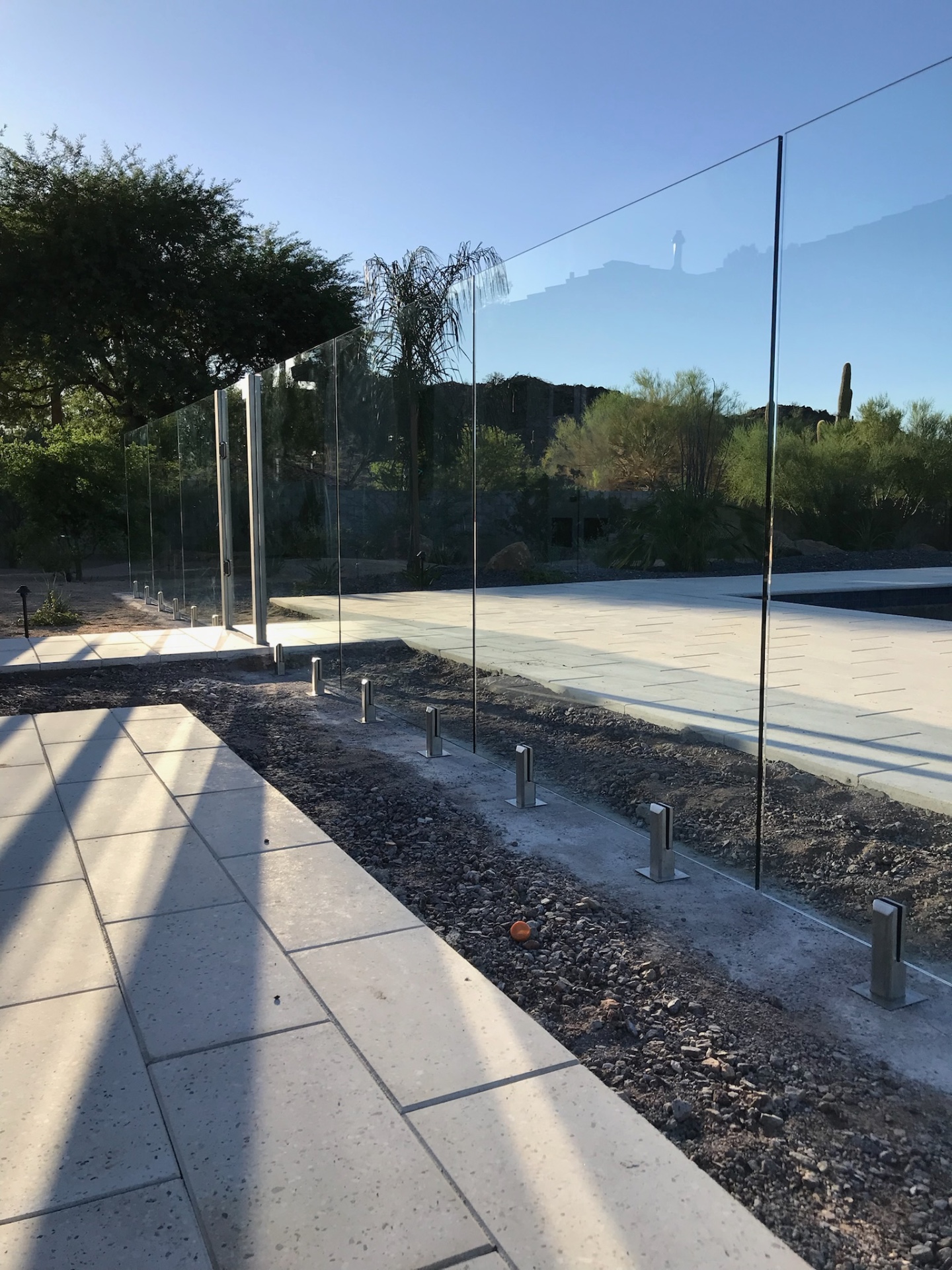 Expansive run of tempered safety glass fence panels reflecting the deep blue Arizona sky and surrounding foothill landscape.