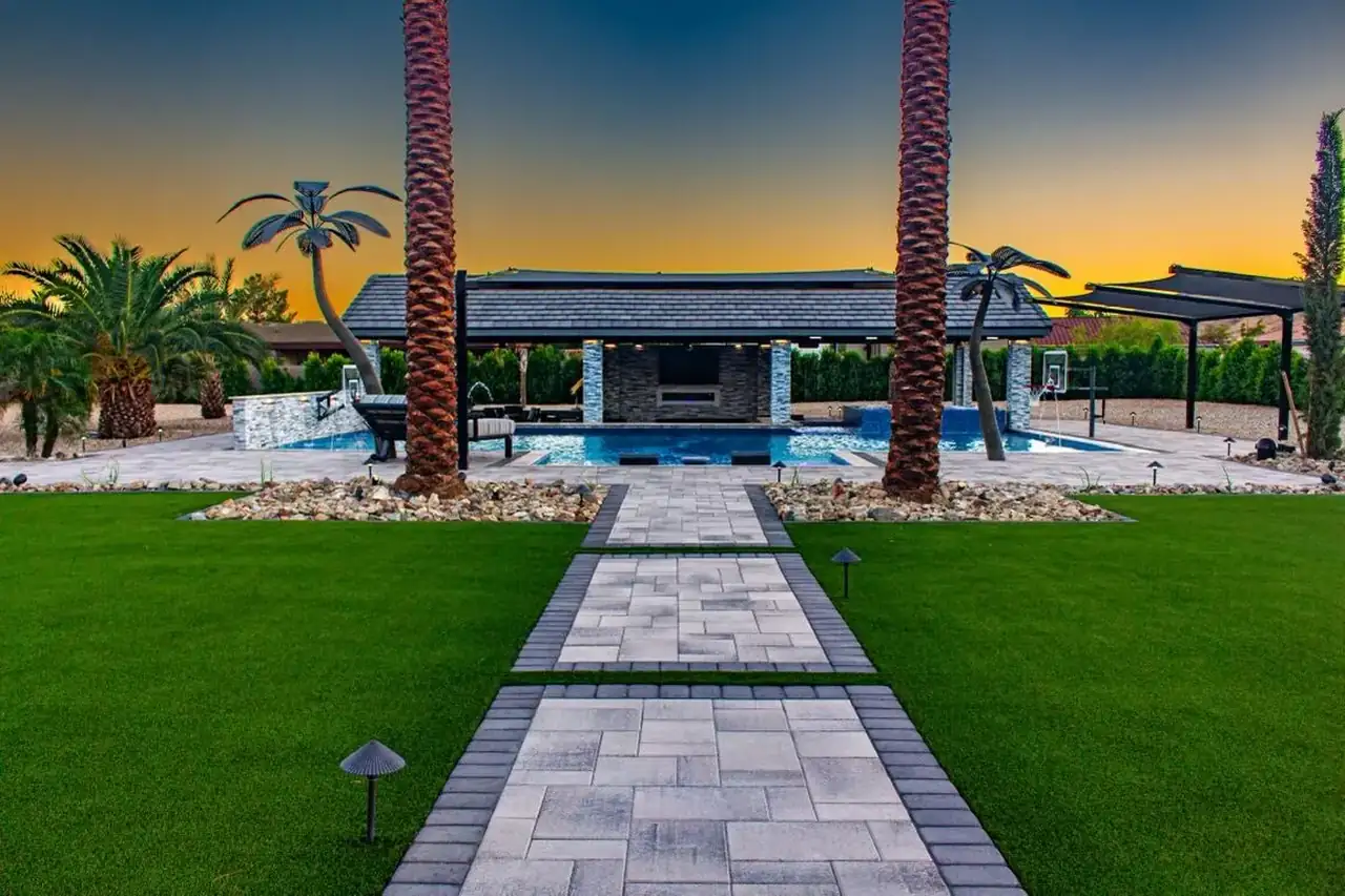 An AE Outdoor Living backyard at sunset — pool, pavers, and landscape lighting in Arizona