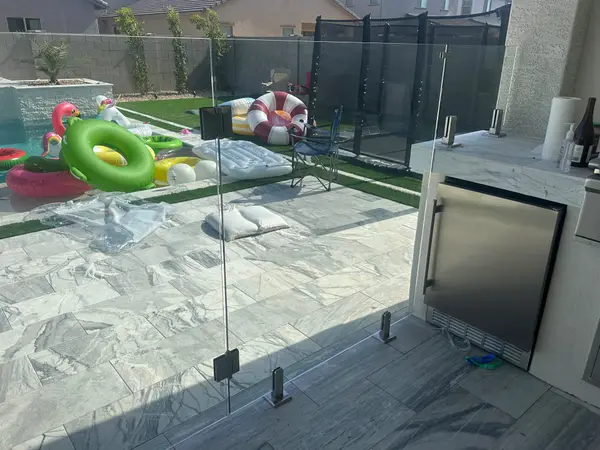 Glass fence panels enclosing the pool deck and outdoor kitchen area with marble-look porcelain pavers — Scottsdale glass fencing install.